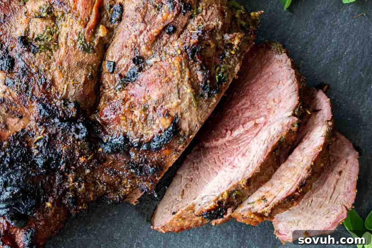 Close-up of a roasted beef cut on a dark surface, partially sliced to show the juicy and tender interior.