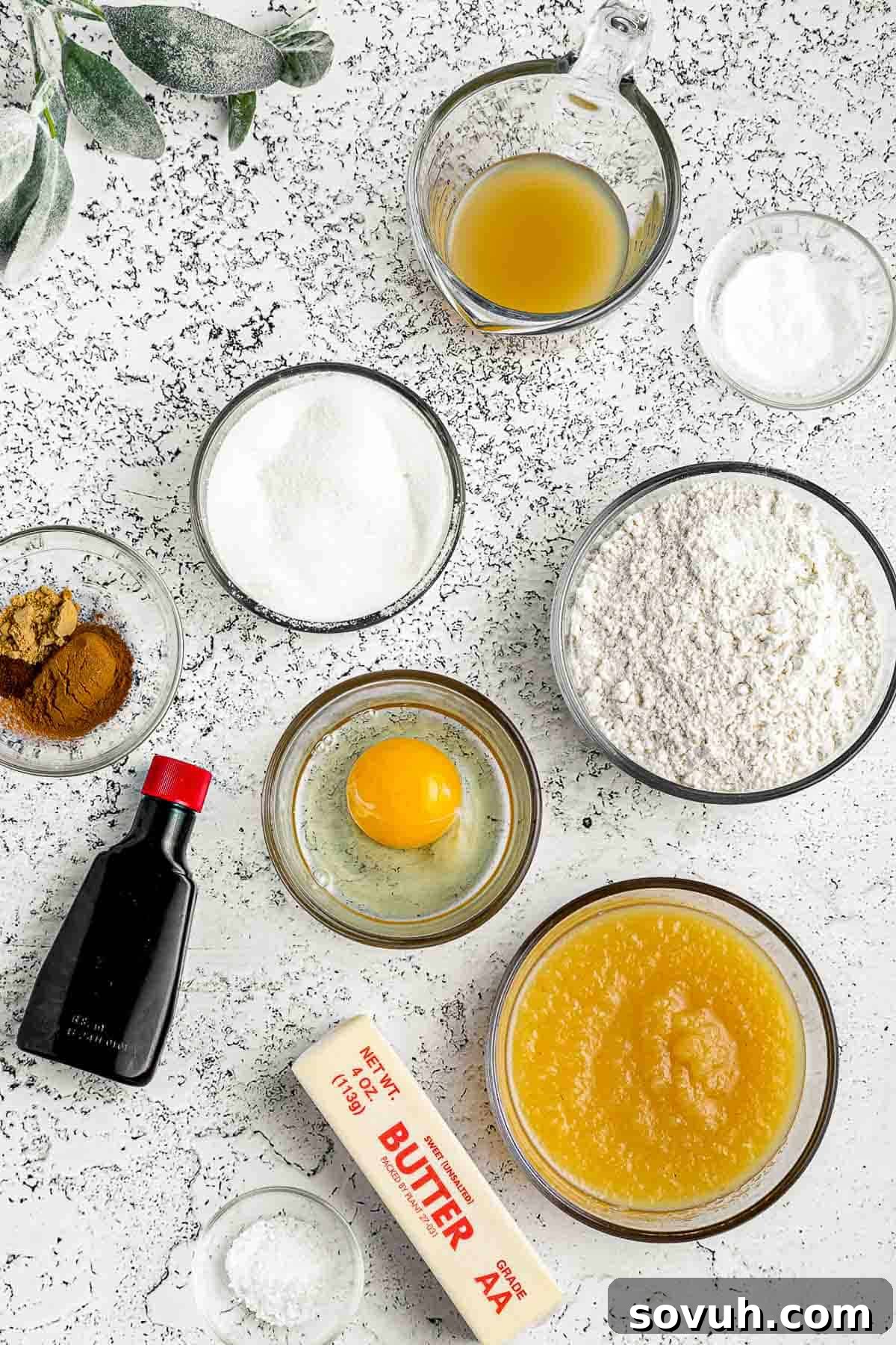 A selection of fresh ingredients laid out on a kitchen counter, showcasing the components needed to bake a delicious Apple Spice Cake. These include flour, sugar, applesauce, butter, apple cider, eggs, and various spices.