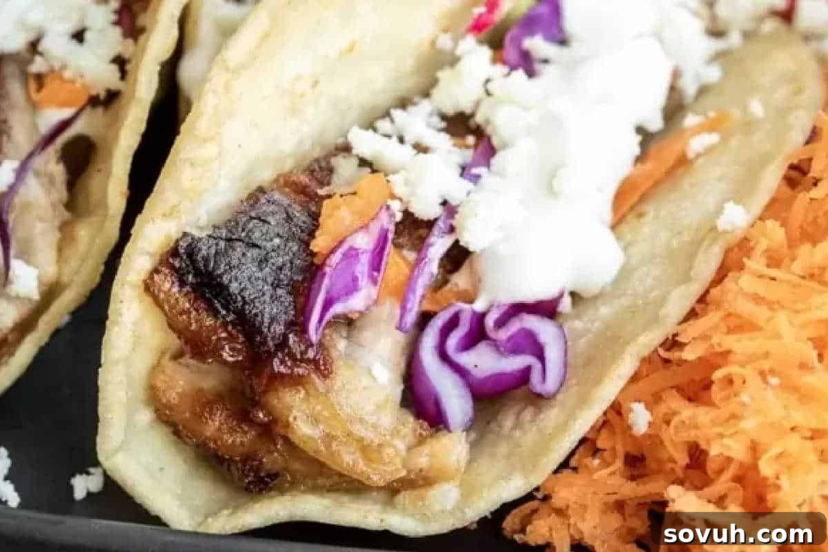 A close-up of a taco with shredded meat, purple cabbage, crumbled cheese, and shredded carrots on the side.
