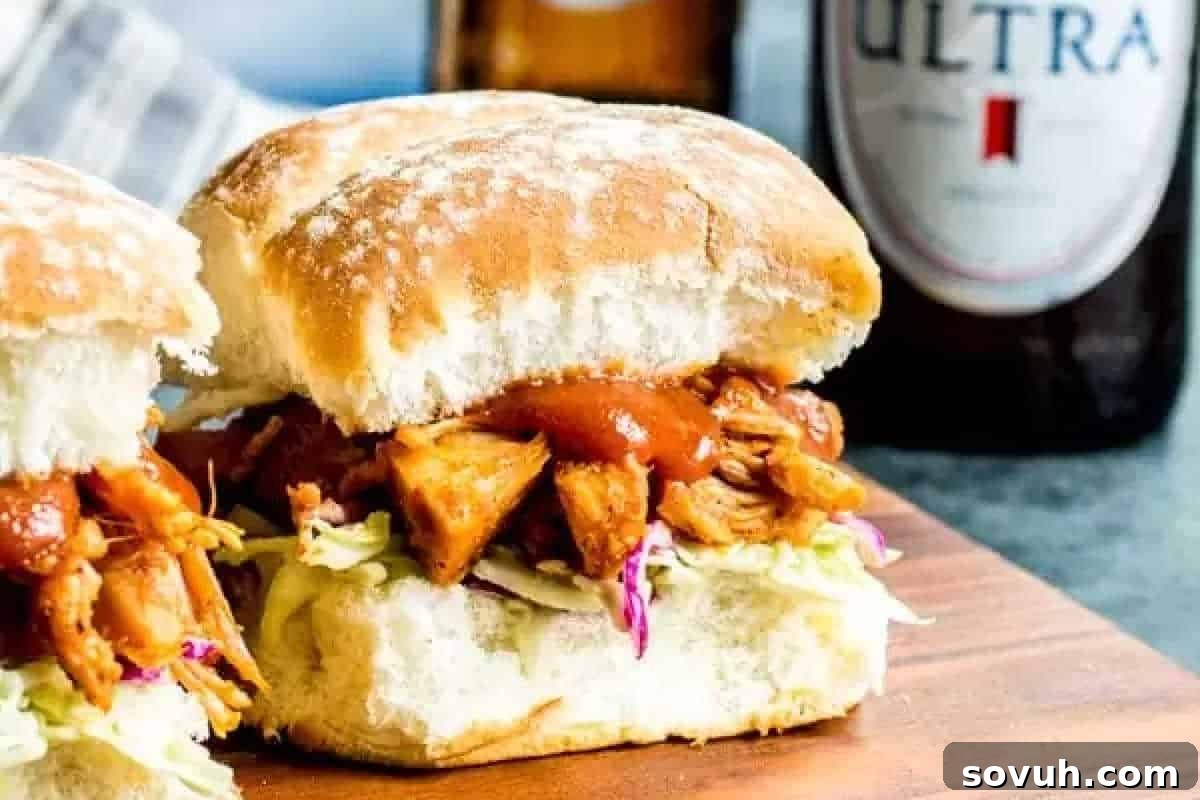 Two barbecue chicken sliders with coleslaw on a wooden surface, with a bottle of beer in the background.