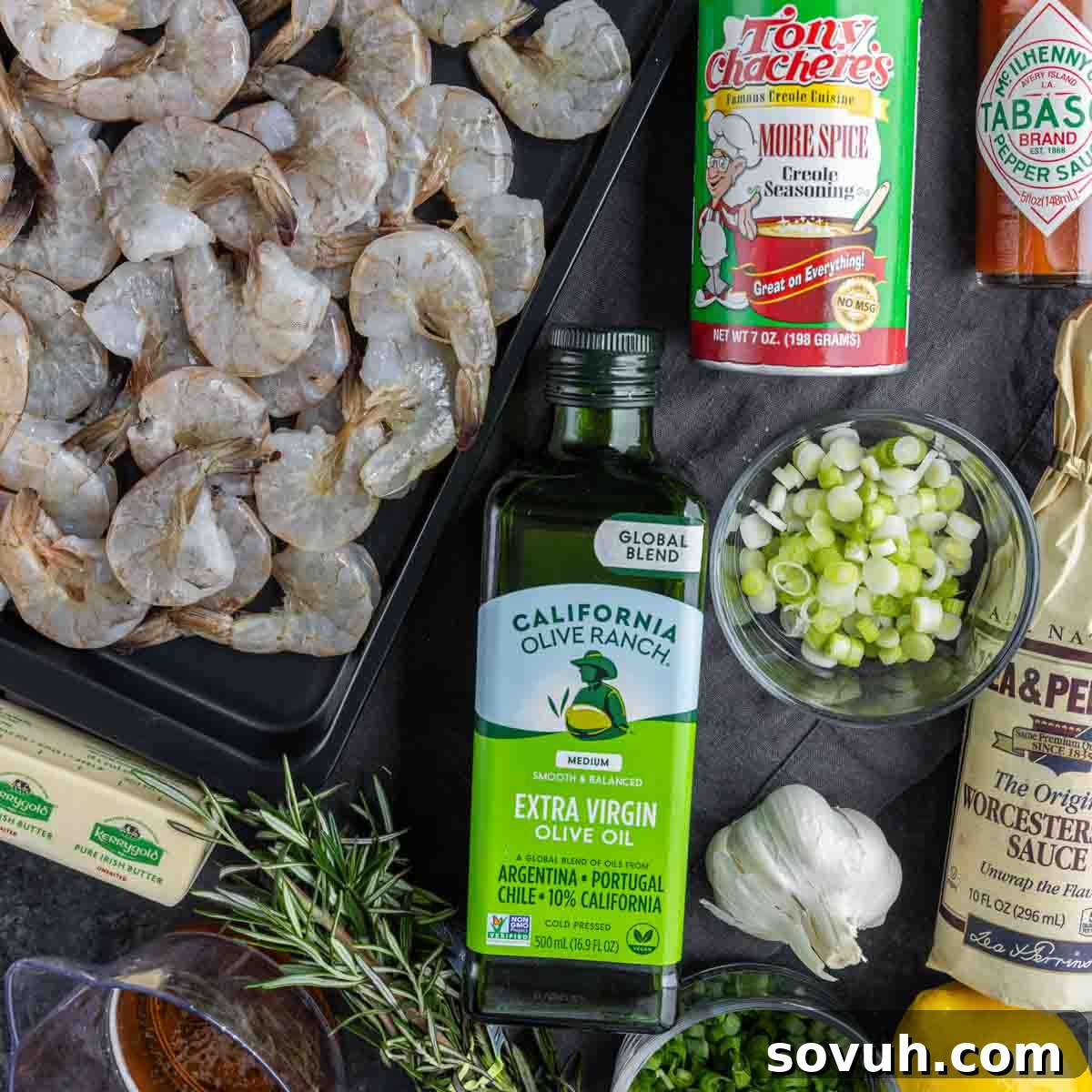 A collection of ingredients including raw shrimp, olive oil, green onions, seasoning, garlic, a lemon, sourdough bread, rosemary, butter, and Tabasco sauce are arranged on a dark surface to make New Orleans BBQ Shrimp