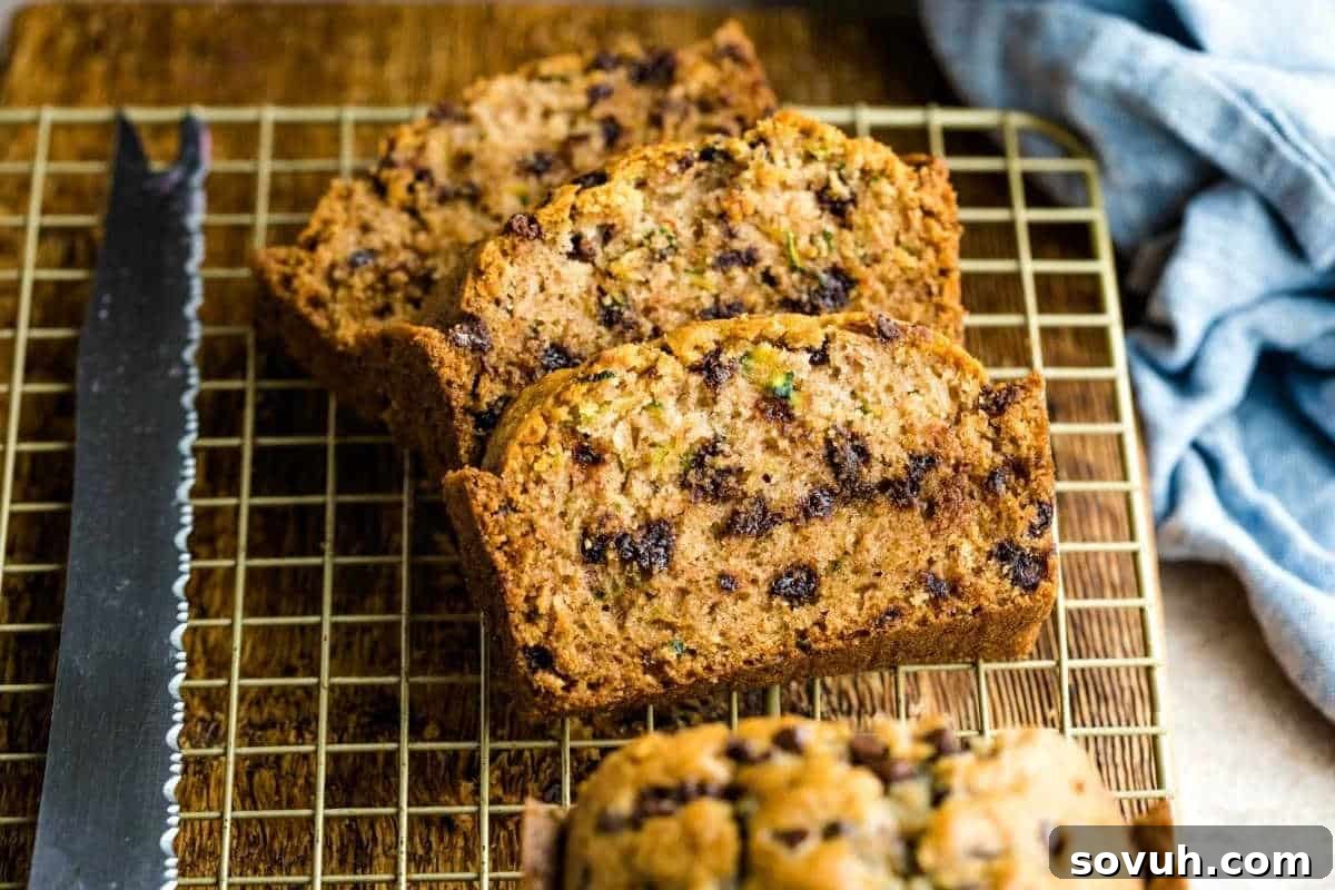Slices of zucchini bread with chocolate chips on a cooling rack next to a serrated knife.