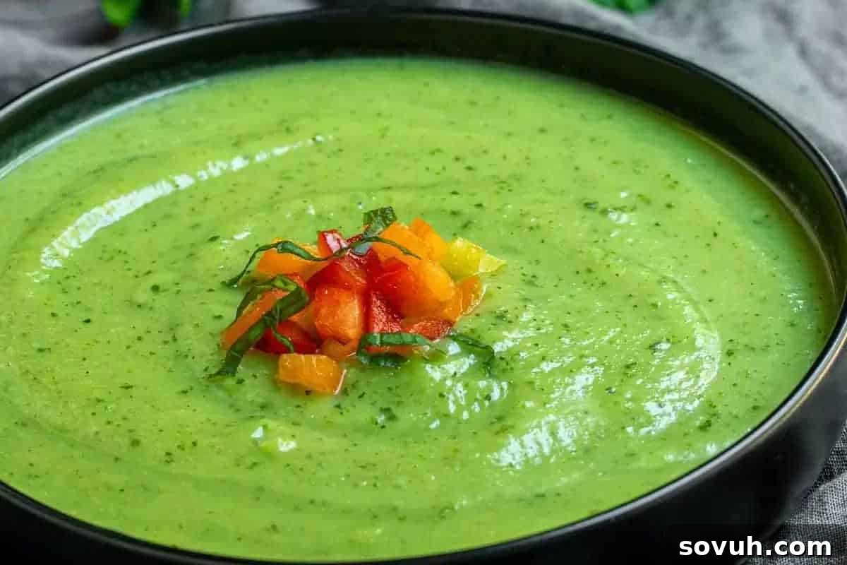 A bowl of green soup garnished with finely chopped red, orange, and yellow vegetables and herbs.