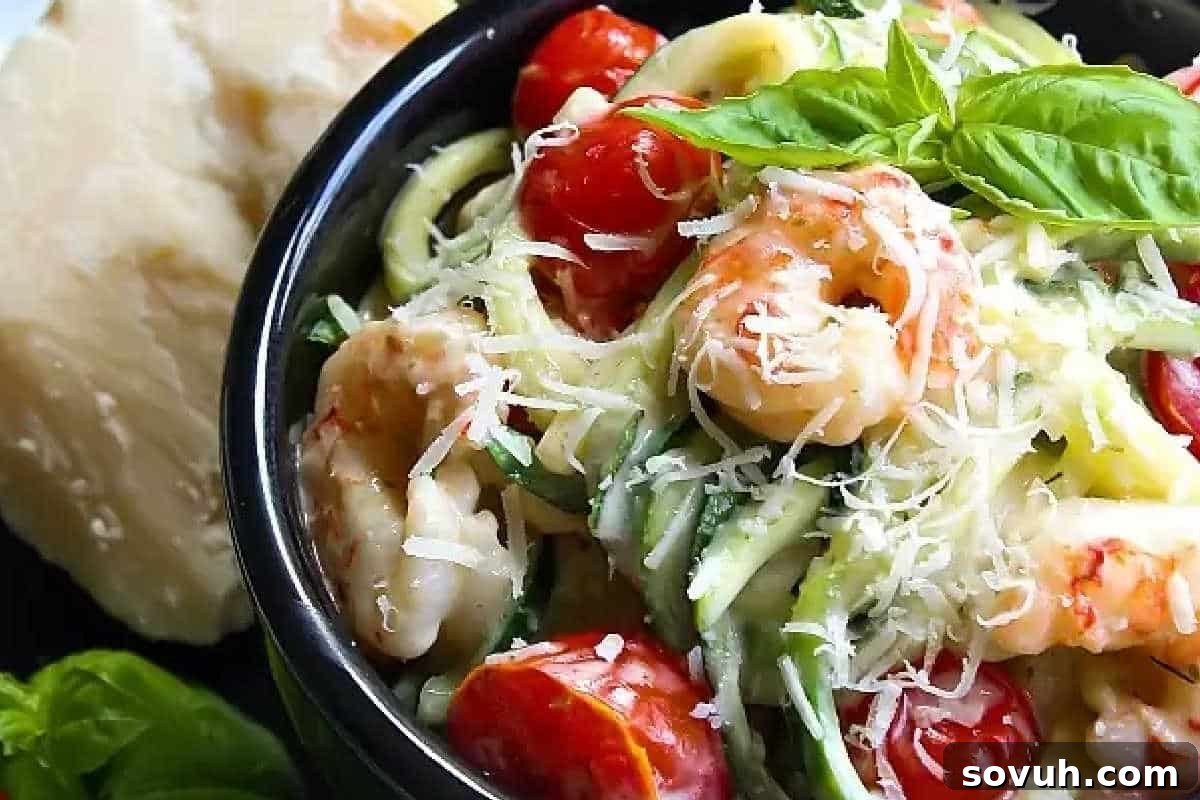 A bowl of shrimp pasta topped with halved cherry tomatoes, grated cheese, and fresh basil leaves. A block of cheese is visible in the background.