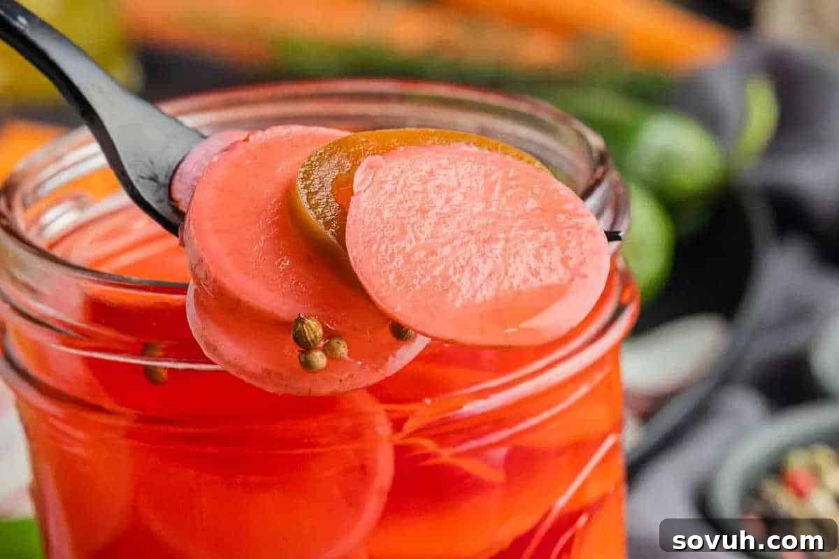 A close-up of a fork holding slices of pickled radish and jalapeño above an open jar, with other vegetables in the blurred background.