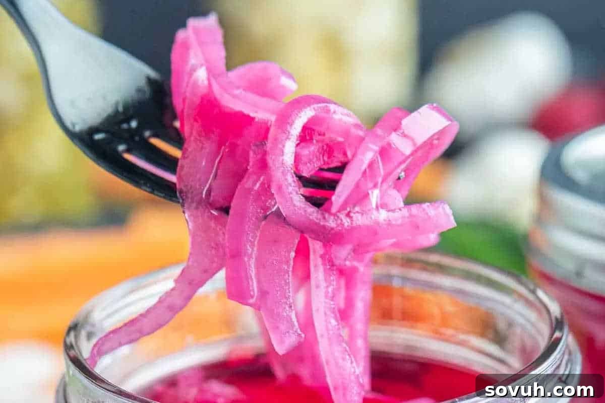 A black fork holds a bunch of thinly sliced pickled red onions above an open glass jar.