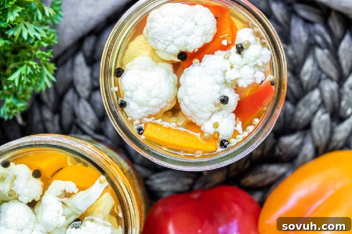 Close-up view of a jar filled with pickled cauliflower, yellow and red bell peppers, and black peppercorns.
