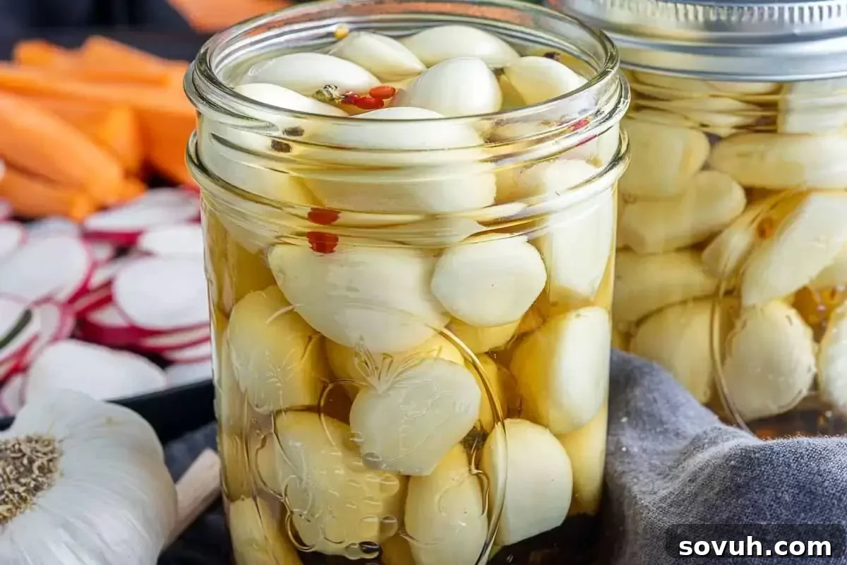 Two jars of pickled garlic cloves in brine, sealed with metal lids, with sliced vegetables and a whole garlic bulb in the background.