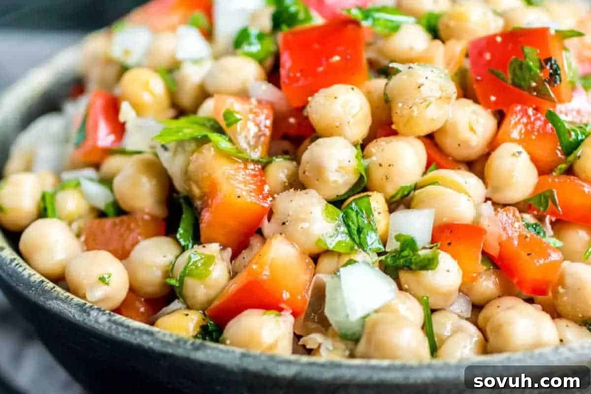 A colorful bowl of chickpea salad brimming with diced red bell peppers, chopped onions, and fresh parsley, all seasoned with cracked black pepper for a Mediterranean flair.