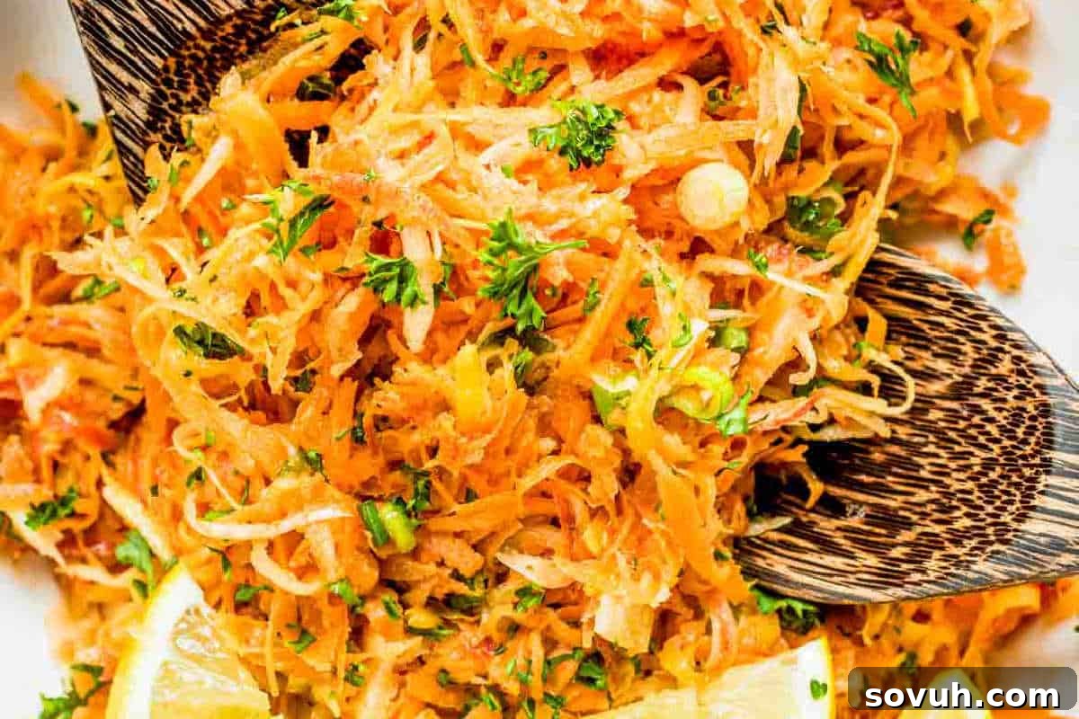 Close-up of a vibrant carrot salad garnished with freshly chopped parsley and bright lemon wedges, served alongside elegant wooden salad tongs.