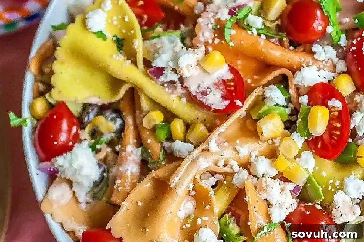 Close-up of a festive pasta salad featuring colorful bowtie pasta, sweet cherry tomatoes, corn, crumbled cheese, finely chopped red onions, and vibrant green peppers, all garnished with fresh herbs for a Tex-Mex flair.