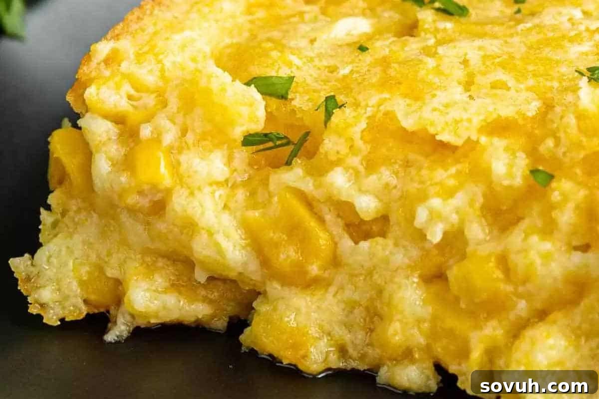 A close-up of a golden-brown, baked corn casserole with visible tender corn kernels and a wonderfully creamy texture, delicately garnished with small green herbs.