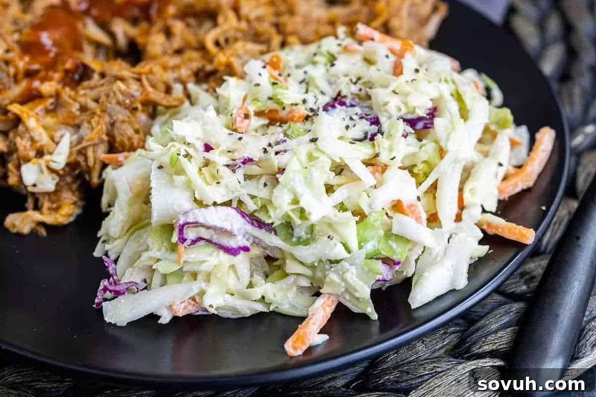 A black plate showcasing a generous serving of classic coleslaw, made with finely shredded cabbage, carrots, and other vegetables, beside a portion of pulled pork with barbecue sauce.
