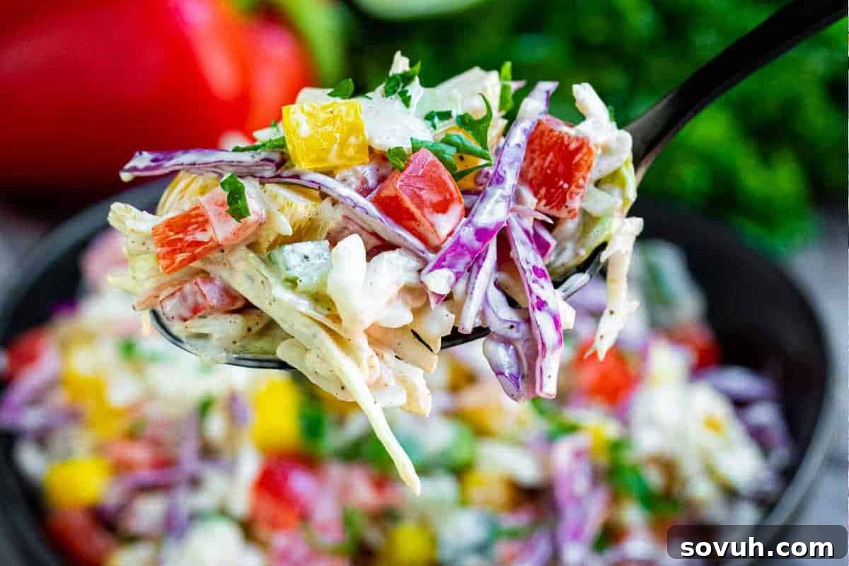 A close-up of a spoonful of coleslaw featuring shredded cabbage, red bell pepper, yellow bell pepper, and a creamy dressing. The bowl of coleslaw is visible in the background.