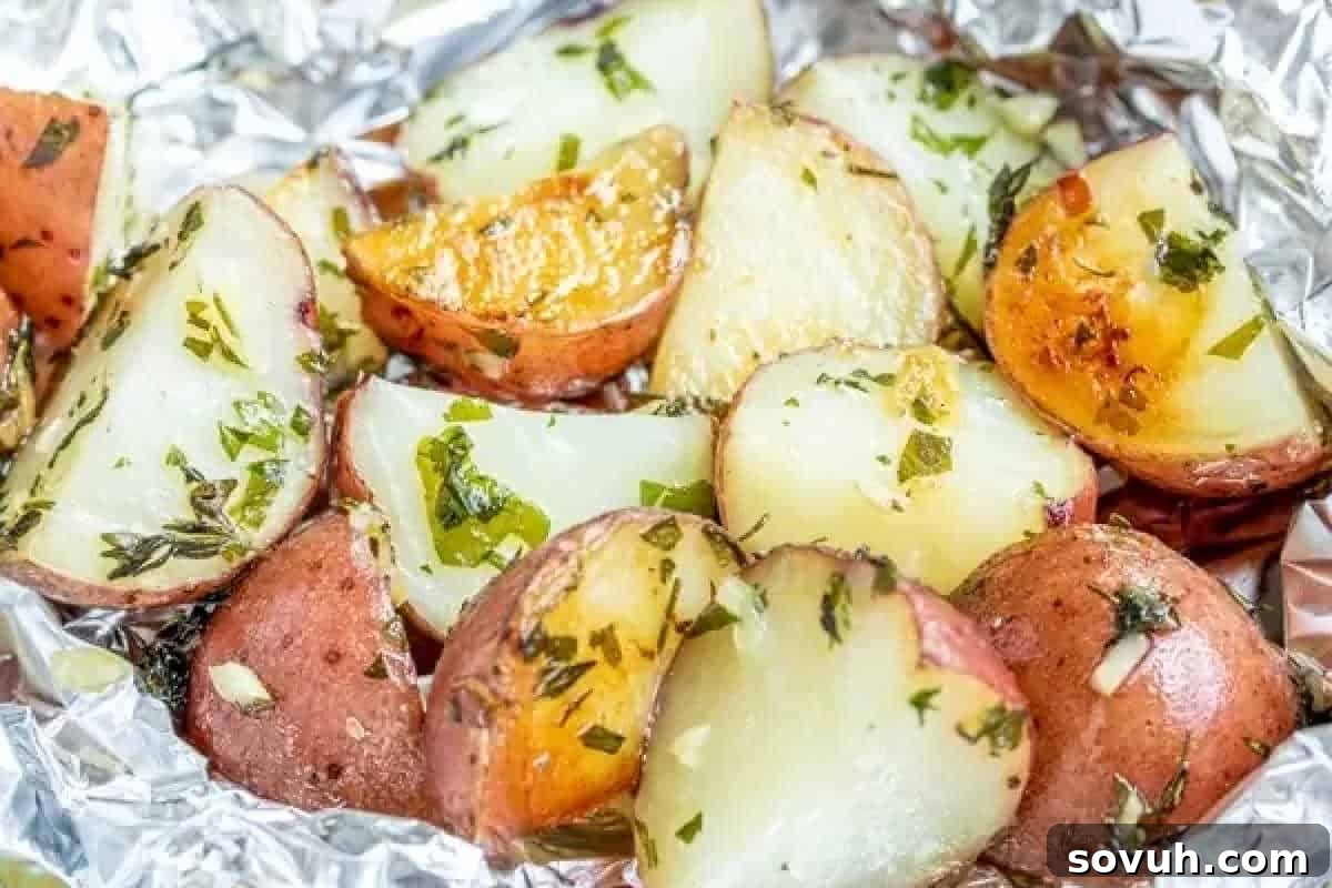 Close-up of roasted potato wedges with herbs and seasonings on aluminum foil.