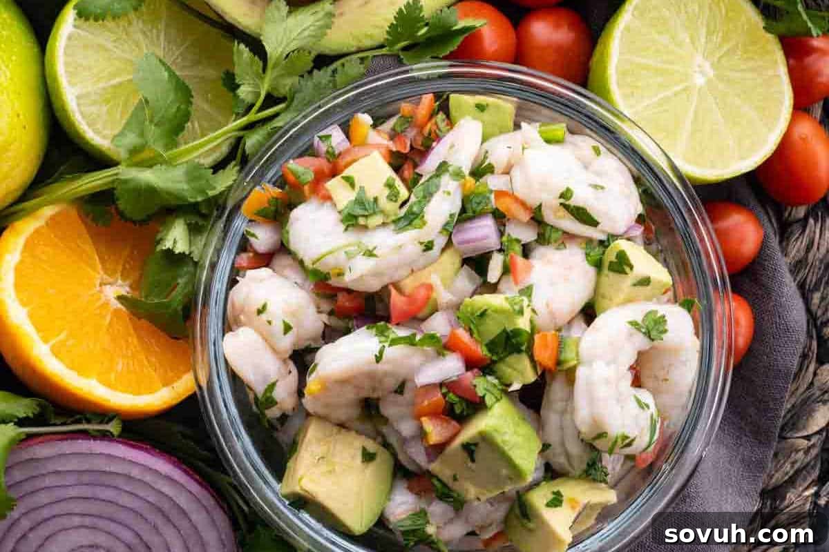 A bowl of shrimp ceviche with avocado, red onions, tomatoes, cilantro, and lime surrounded by fresh lime, lemon, orange slices, and more vegetables.