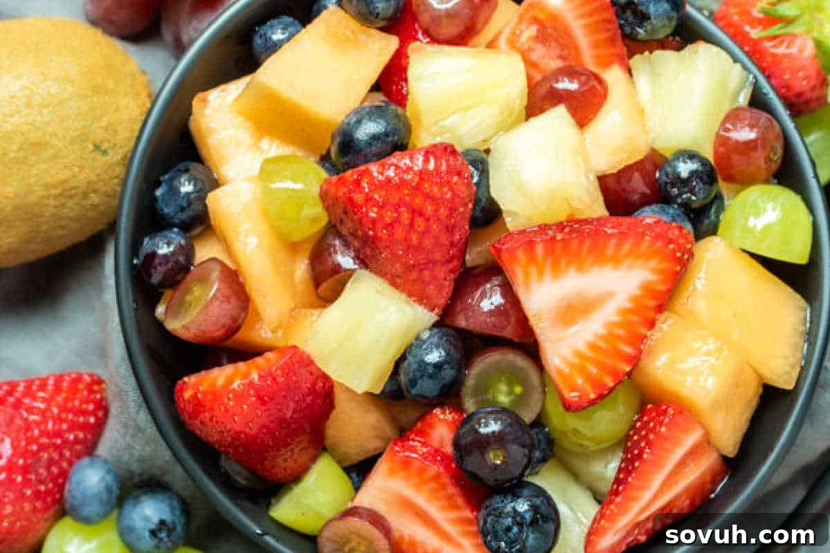 A close-up image of a bowl filled with a colorful assortment of fresh fruit, including strawberries, blueberries, grapes, pineapple, and cantaloupe.