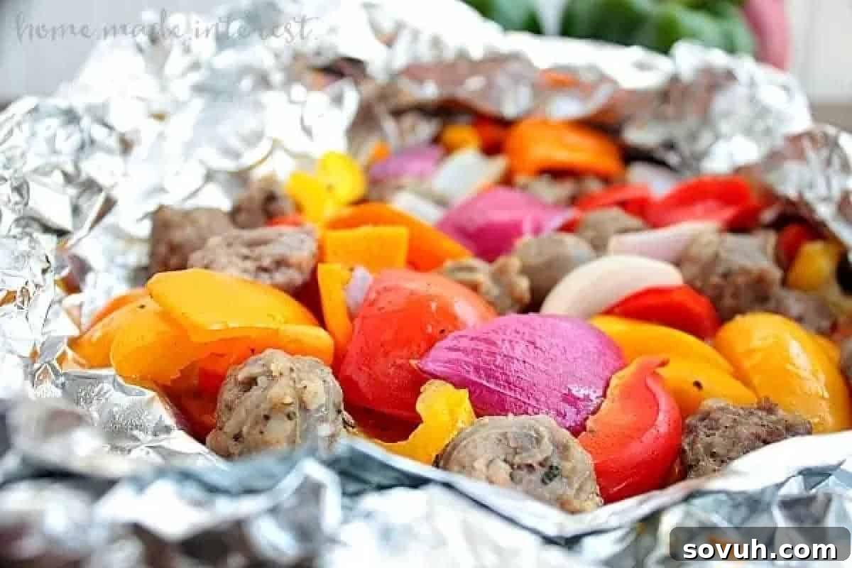 A foil packet filled with cooked sausage pieces, red onions, and colorful bell peppers.