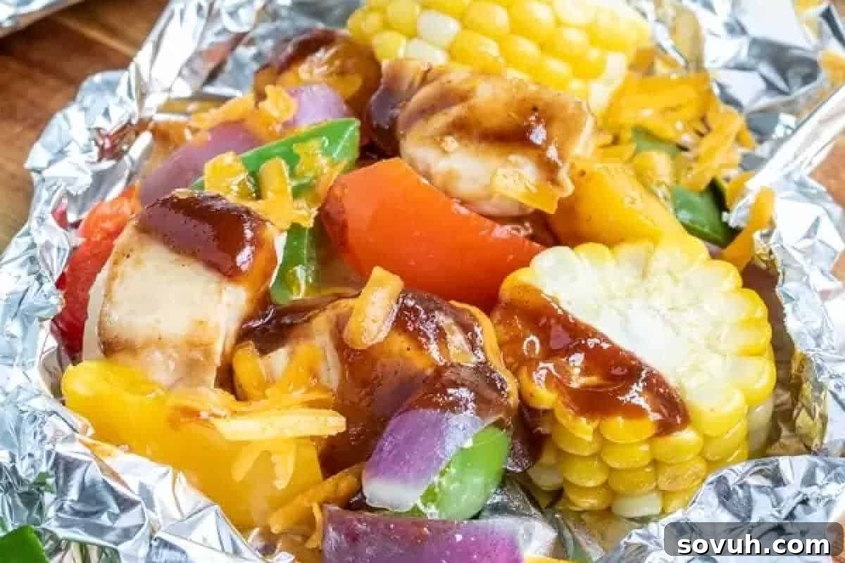 A foil packet containing a mix of grilled vegetables, corn on the cob pieces, and sauced chicken chunks.