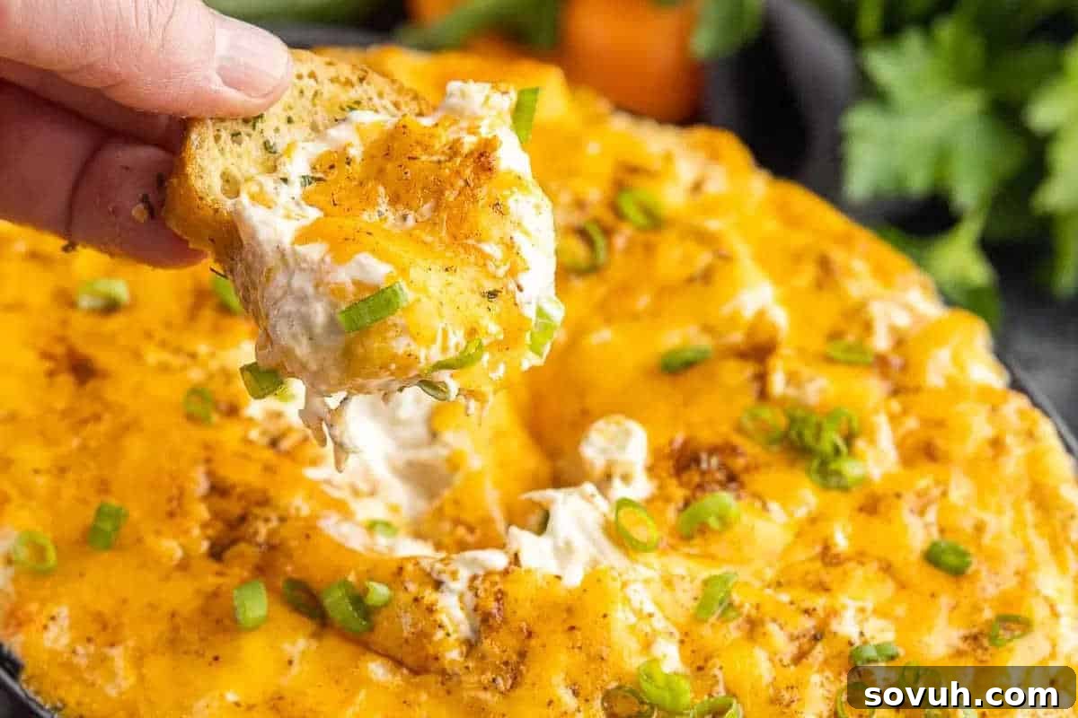 A tantalizing image of a hand expertly dipping a piece of crusty garlic bread into a bubbling, cheesy crab dip, generously topped with vibrant green onions and a sprinkle of seasoning. The dish is presented on a wooden surface.