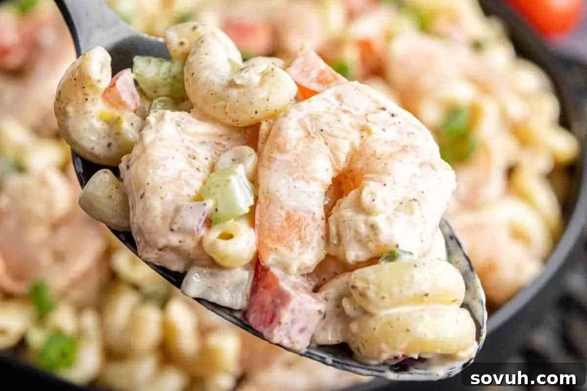 A close-up shot of a spoonful of vibrant shrimp pasta salad, featuring tender elbow macaroni, succulent shrimp, crisp diced red bell peppers, and fresh celery, all coated in a rich, creamy dressing.