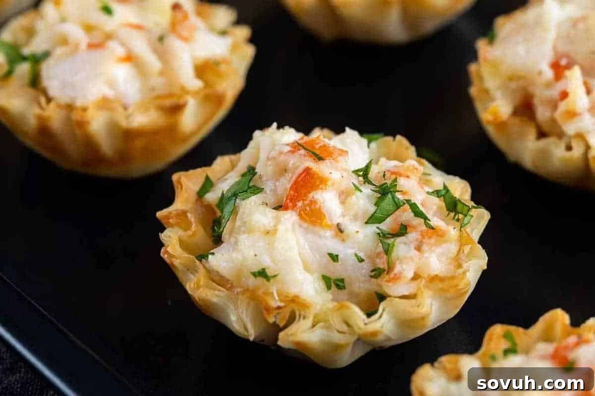 Four golden-brown phyllo pastry cups, each exquisitely filled with a creamy crab mixture and delicately garnished with chopped fresh parsley, presented on an elegant black serving tray.