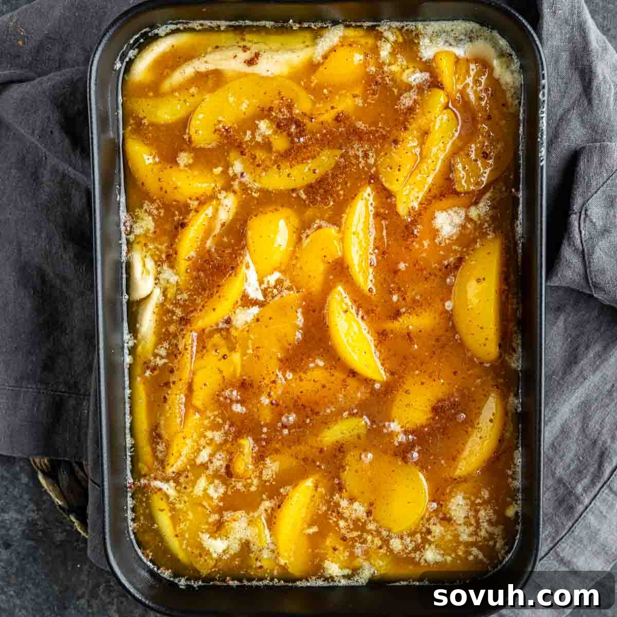 A rectangular baking dish filled with an unbaked peach cobbler, showcasing carefully arranged peach slices layered over a smooth, golden-brown batter, ready for the oven.
