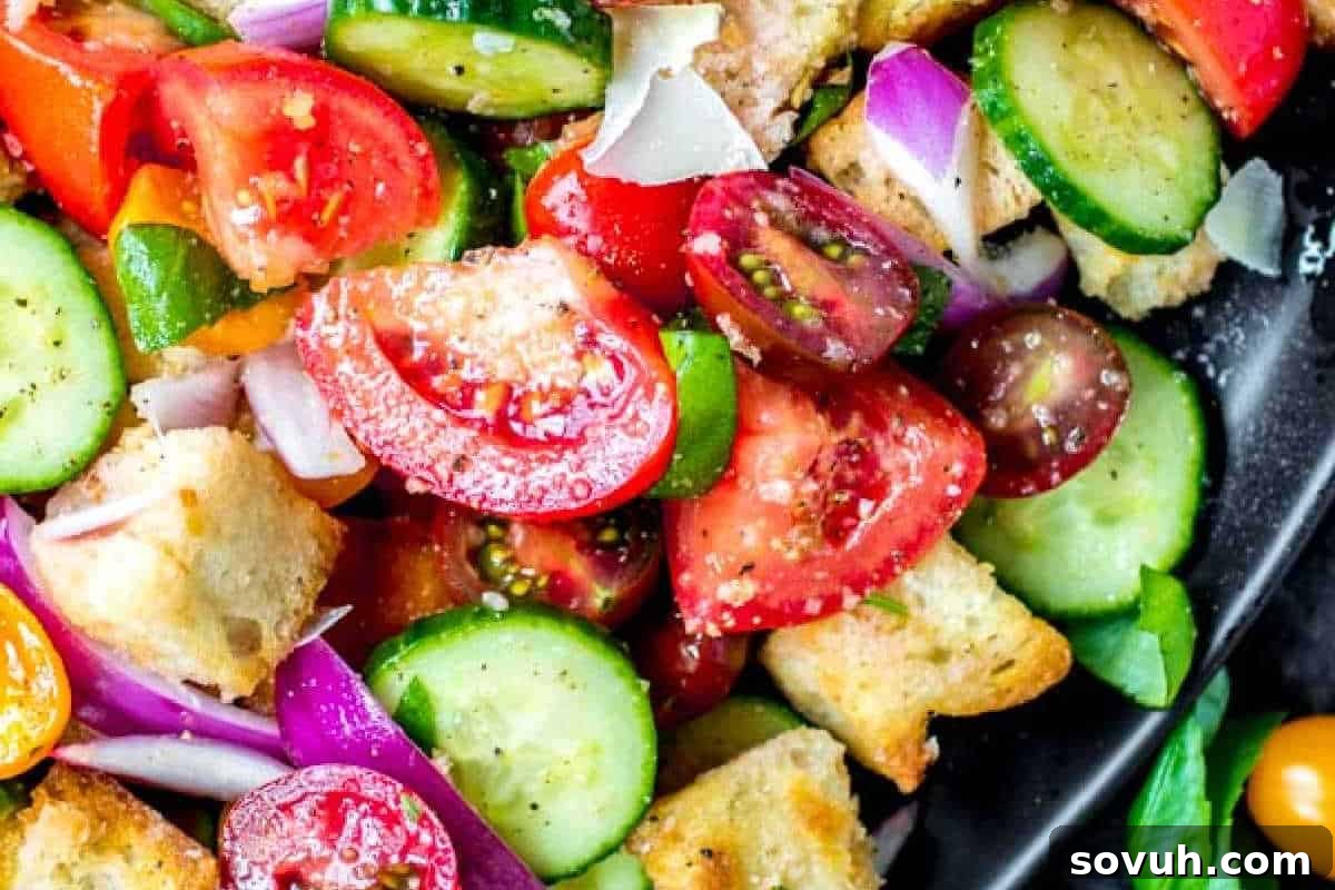 Close-up of a vegetable salad featuring chopped tomatoes, cucumbers, red onions, and croutons, served in a black bowl.
