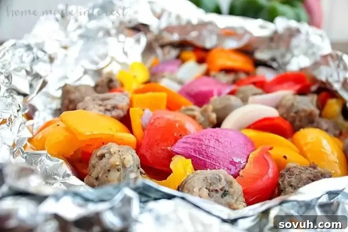 A foil packet filled with roasted red, orange, and yellow bell peppers, red onions, and sausage pieces.