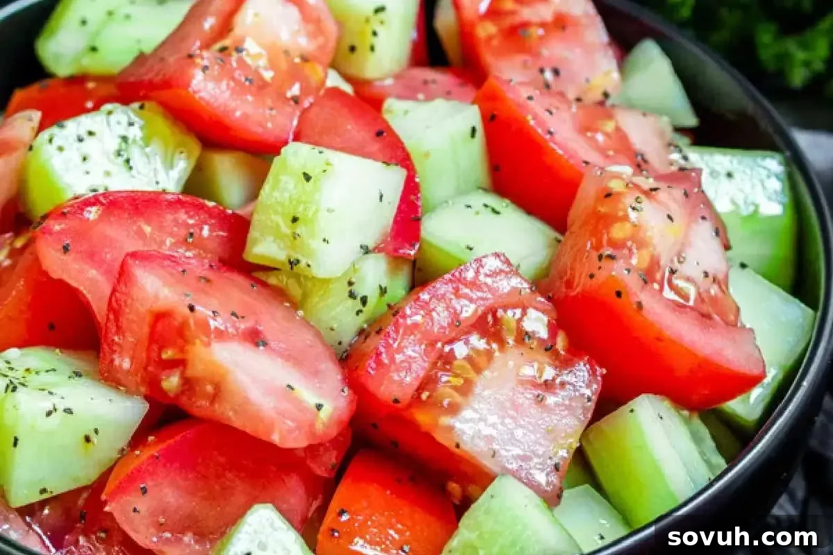 A close-up of a salad bowl filled with chunks of tomatoes and cucumbers, lightly seasoned with black pepper and herbs.