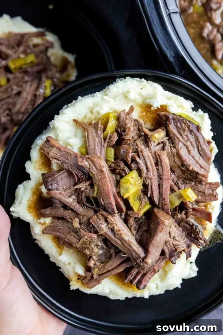 Mississippi Pot Roast: Slow Cooked Southern Charm 5 A plate of fluffy mashed potatoes generously topped with tender Slow Cooker Mississippi Pot Roast, held above a slow cooker filled with more delicious roast.