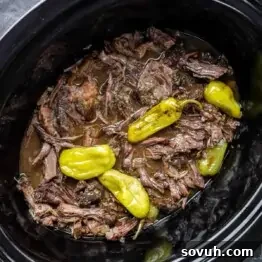 Slow Cooker Mississippi Pot Roast and whole yellow peppers in a brown broth.