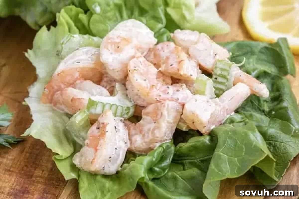 A refreshing dish of creamy Shrimp Salad, featuring perfectly seasoned shrimp and finely sliced celery, elegantly served on a crisp bed of green lettuce and garnished with a bright lemon slice. This light and flavorful salad is perfect for a healthy meal.