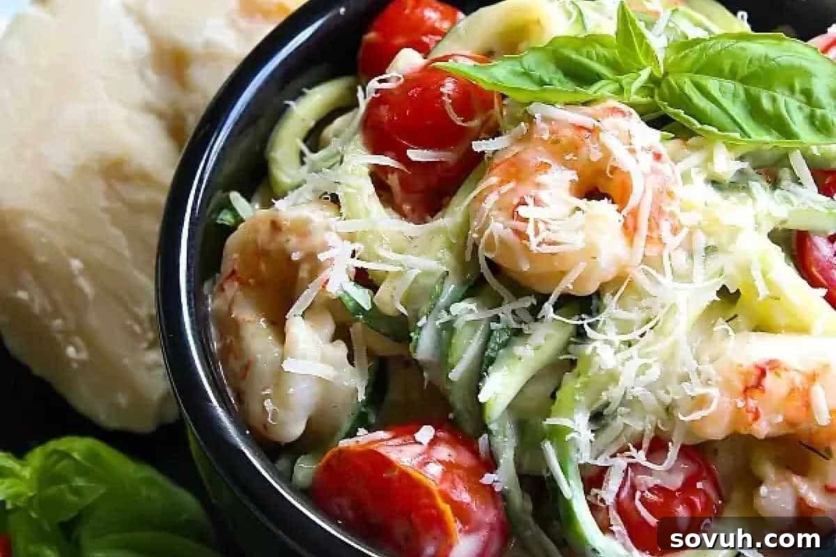 A vibrant, healthy bowl of One Pot Low Carb Shrimp Alfredo featuring succulent shrimp nestled amidst spiraled zucchini noodles, bright cherry tomatoes, and fresh basil leaves, all generously coated in a creamy sauce and topped with grated Parmesan cheese.
