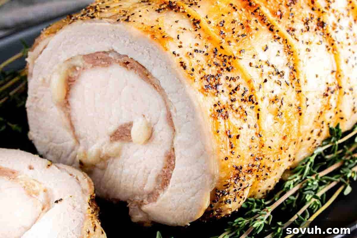 Close-up of a sliced, seasoned, and cooked pork loin garnished with fresh thyme.