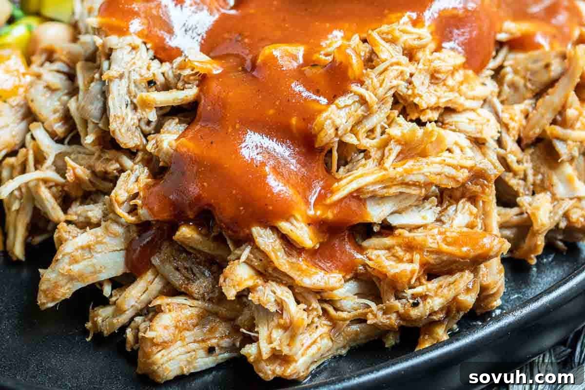 Close-up of shredded barbecue pulled pork drenched in sauce, served on a dark plate.