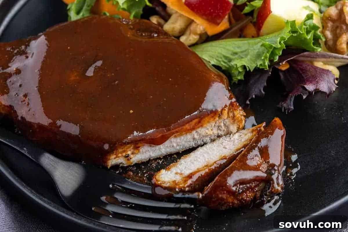 A sliced pork chop covered in brown sauce on a black plate, served with a side salad that includes greens, sliced apples, and some nuts.