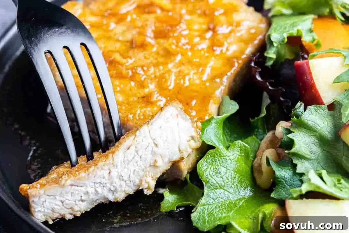A fork cutting into a breaded pork chop served with a side salad featuring leafy greens and apple slices.