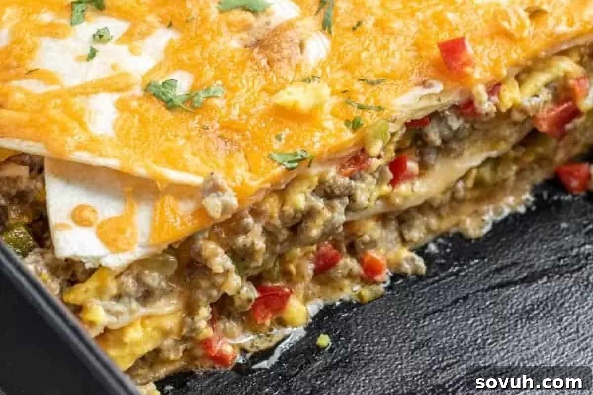 A close-up view of a sliced layered casserole made with melted cheese, ground meat, bell peppers, and tortillas, served on a black surface.