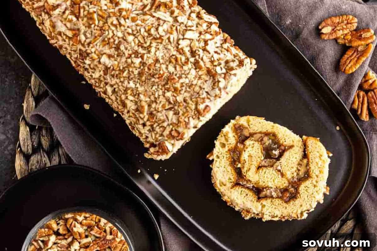 Cake Mix Magic 11 A pecan-encrusted dessert loaf on a black platter with a single slice next to it. A bowl of pecans and additional whole pecans are placed nearby.