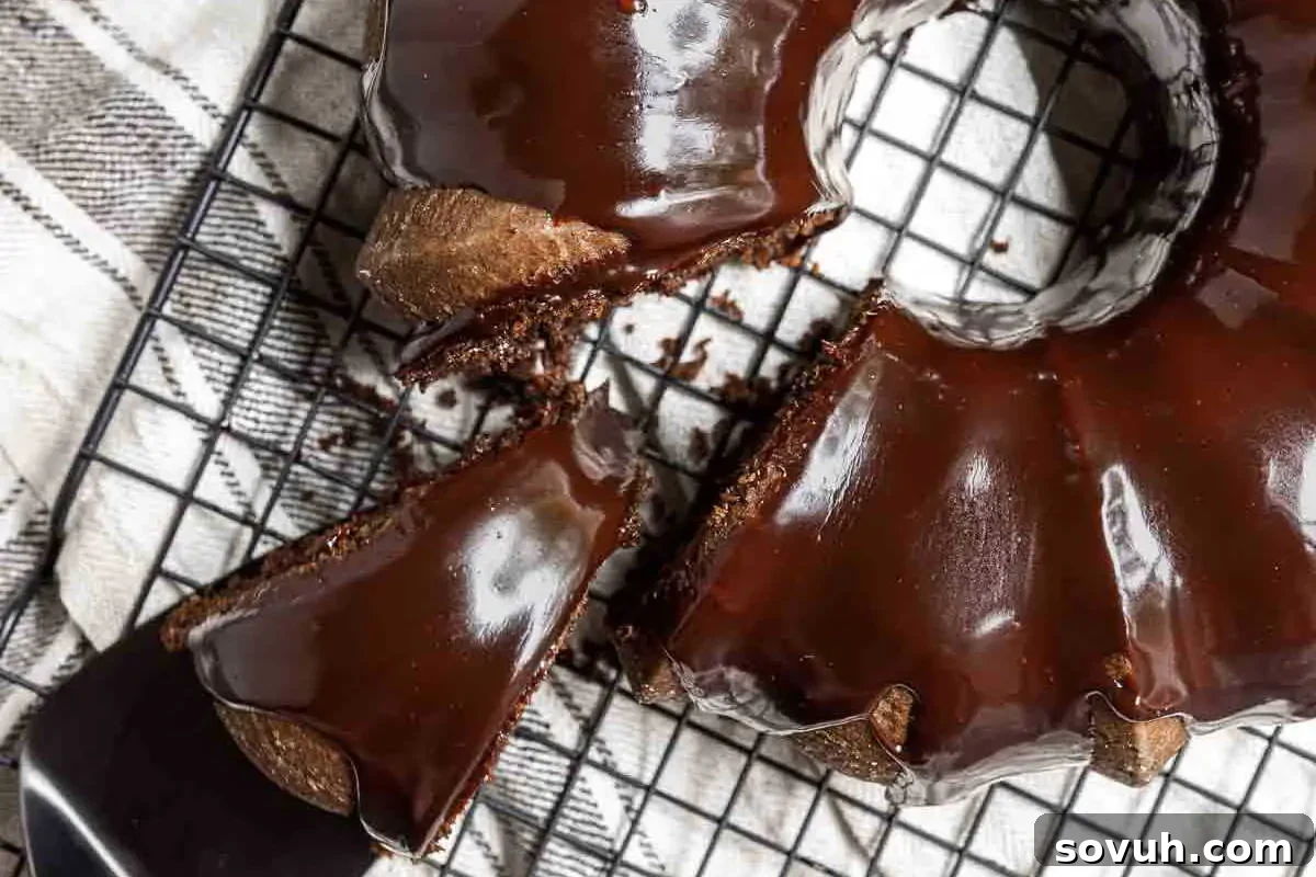 Cake Mix Magic 18 A chocolate bundt cake with glossy icing on a wire rack, with one slice partially cut and a cake server positioned nearby.