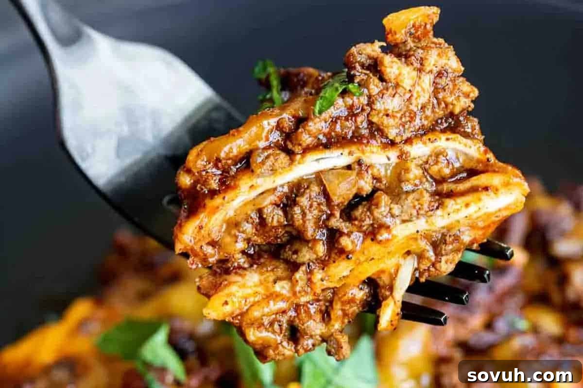 A close-up shot of a fork lifting a perfect piece of beef enchilada casserole, showcasing enticing layers of seasoned ground beef, soft tortillas, rich enchilada sauce, and melted cheese, with a subtle garnish of green herbs.