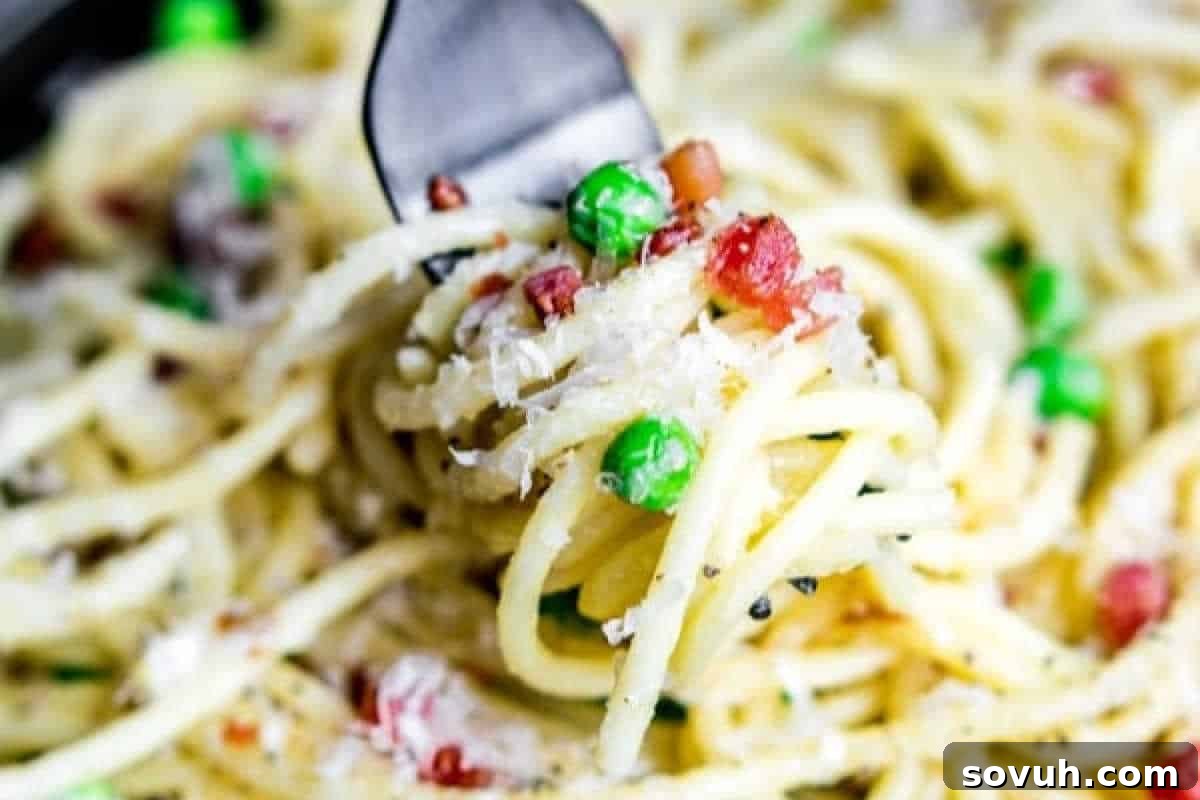 A fork lifts a generous portion of authentic Pasta Carbonara, showcasing perfectly cooked spaghetti coated in a rich, creamy sauce, studded with sweet peas, savory bacon bits, and grated cheese.