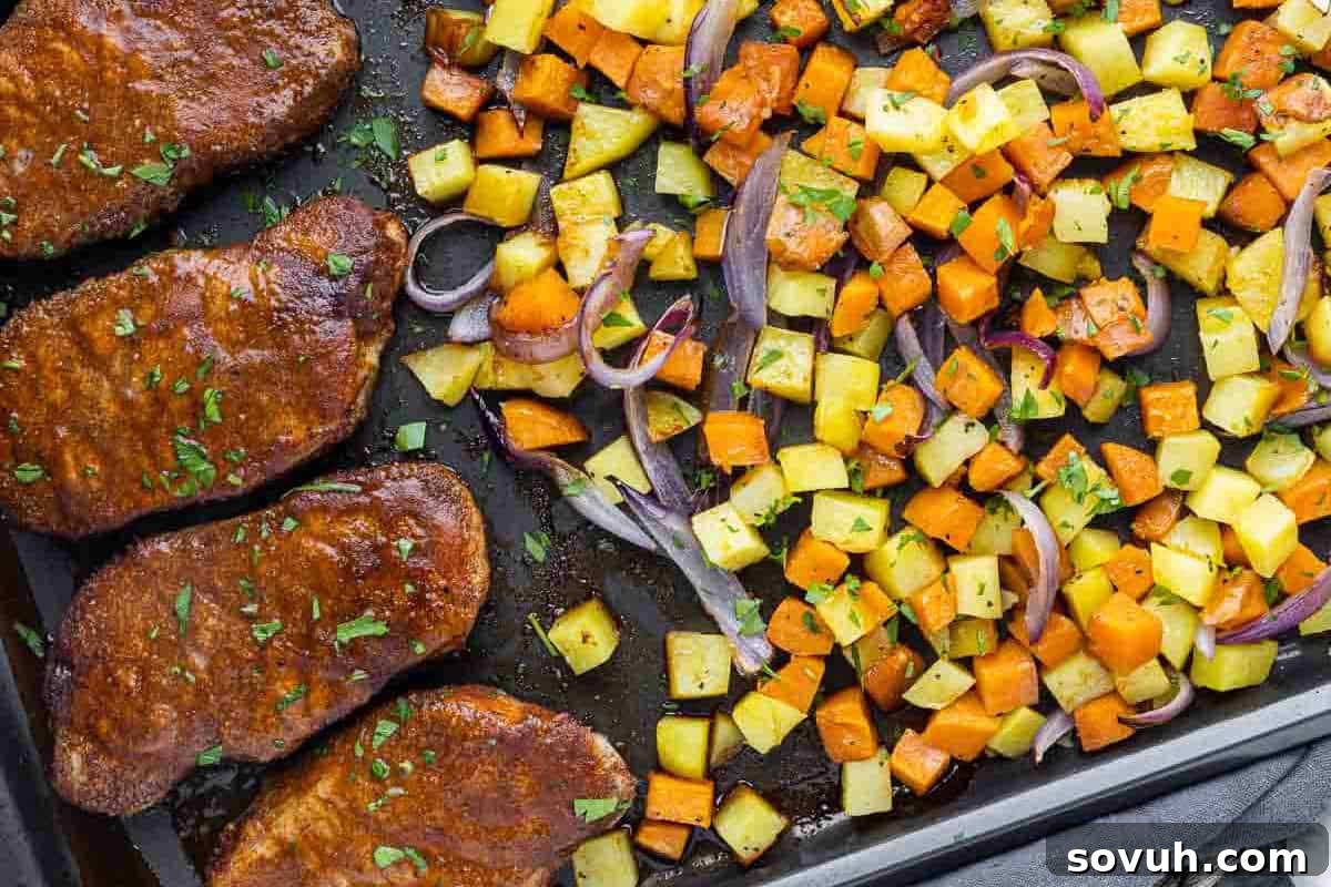 A bustling sheet pan dinner featuring four perfectly cooked spicy BBQ pork chops on one side, paired with a colorful medley of roasted diced potatoes, sweet potatoes, and onions on the other, creating a complete and satisfying meal.
