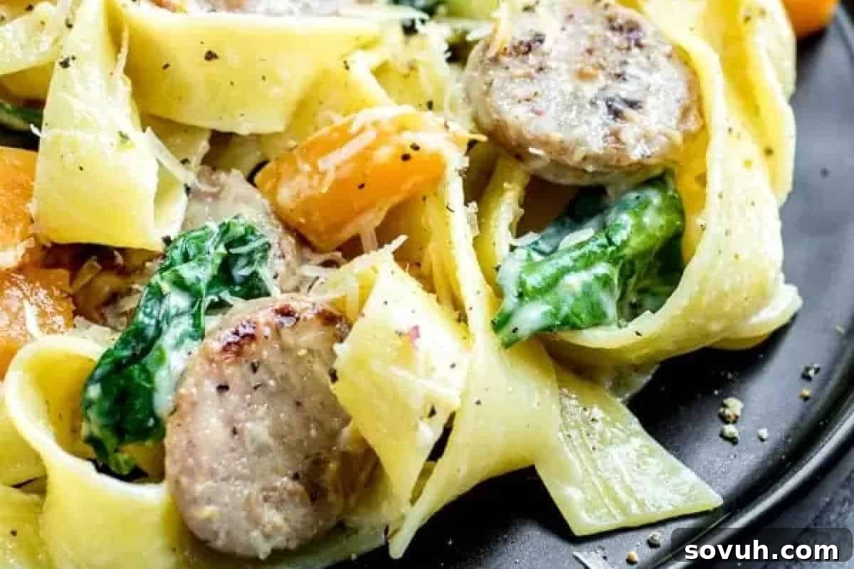 A vibrant pasta dish featuring wide noodles tossed with slices of savory sausage, fresh spinach, and sweet diced yellow bell peppers, generously garnished with grated cheese and a sprinkle of black pepper.