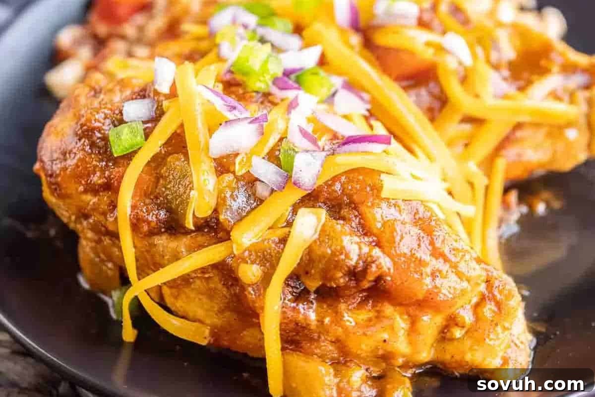 A delectable cooked chicken breast, generously topped with melted shredded cheese, vibrant diced red onions, and fresh chopped green peppers, presented on a sleek black plate.