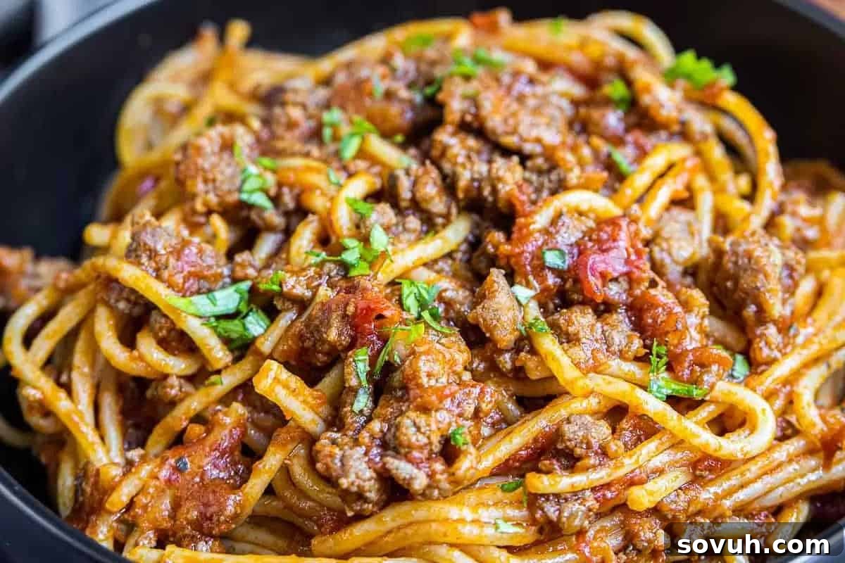 A generous serving of classic spaghetti topped with a rich, savory meat-based tomato sauce, elegantly garnished with fresh chopped parsley, ready to be enjoyed.