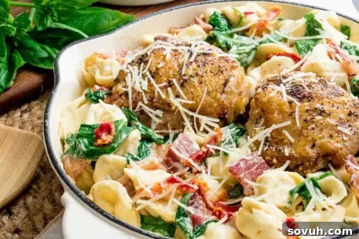 A close-up of a delectable one-pot creamy chicken tortellini dish, showcasing tender grilled chicken thighs, plump cheese tortellini, vibrant spinach, juicy sun-dried tomatoes, and crispy bacon bits, all coated in a rich, cheesy sauce and topped with grated Parmesan.