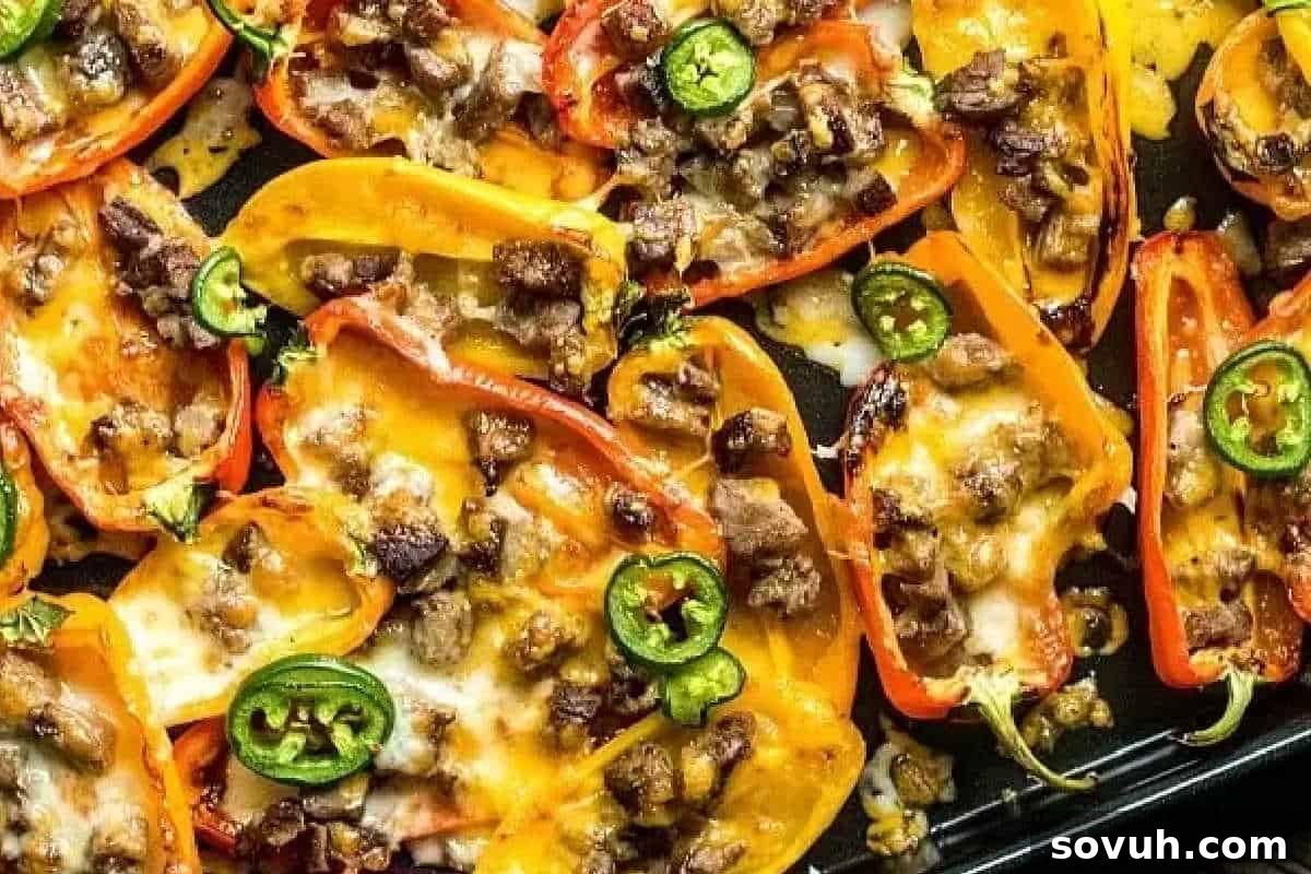 Baked bell pepper halves topped with melted cheese, diced meat, and slices of jalapeño on a baking tray.
