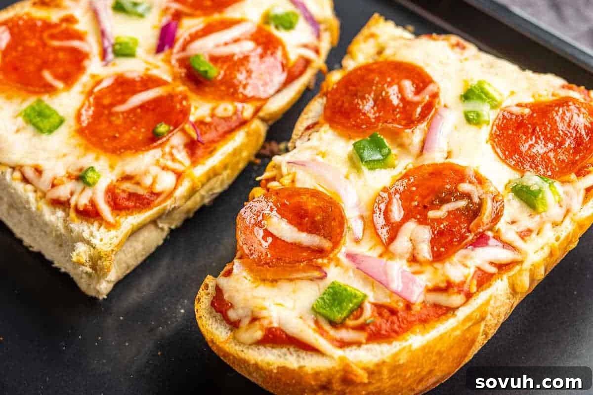 Close-up of French bread pizza slices topped with melted cheese, pepperoni, green bell peppers, and red onions on a dark surface.